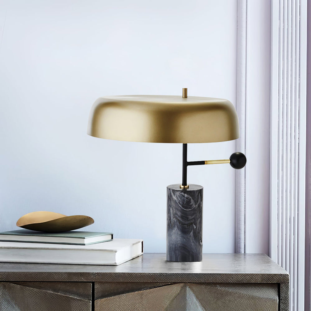 Gold-shade table lamp on a textured cabinet beside stacked books and a curved gold-tone ornament