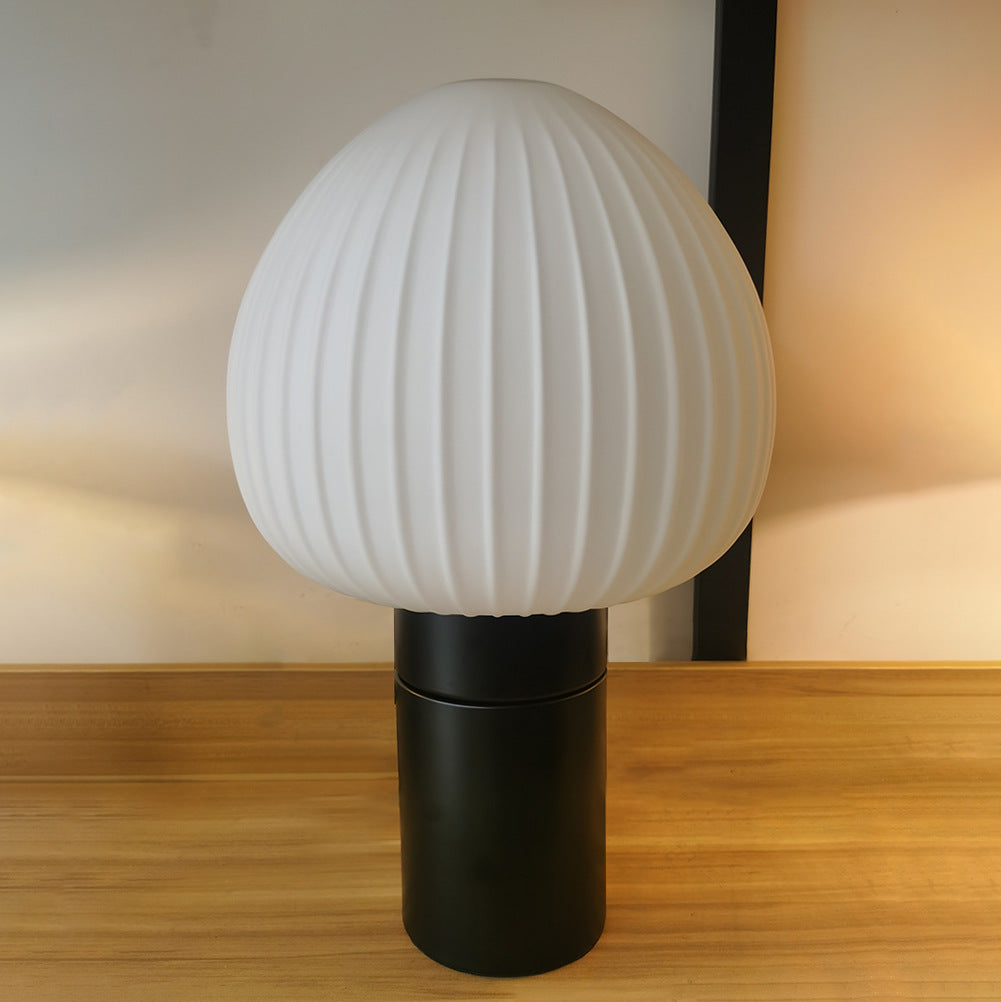 Close front view of the rounded white shade with vertical ribs and smooth black cylindrical base on a wood surface