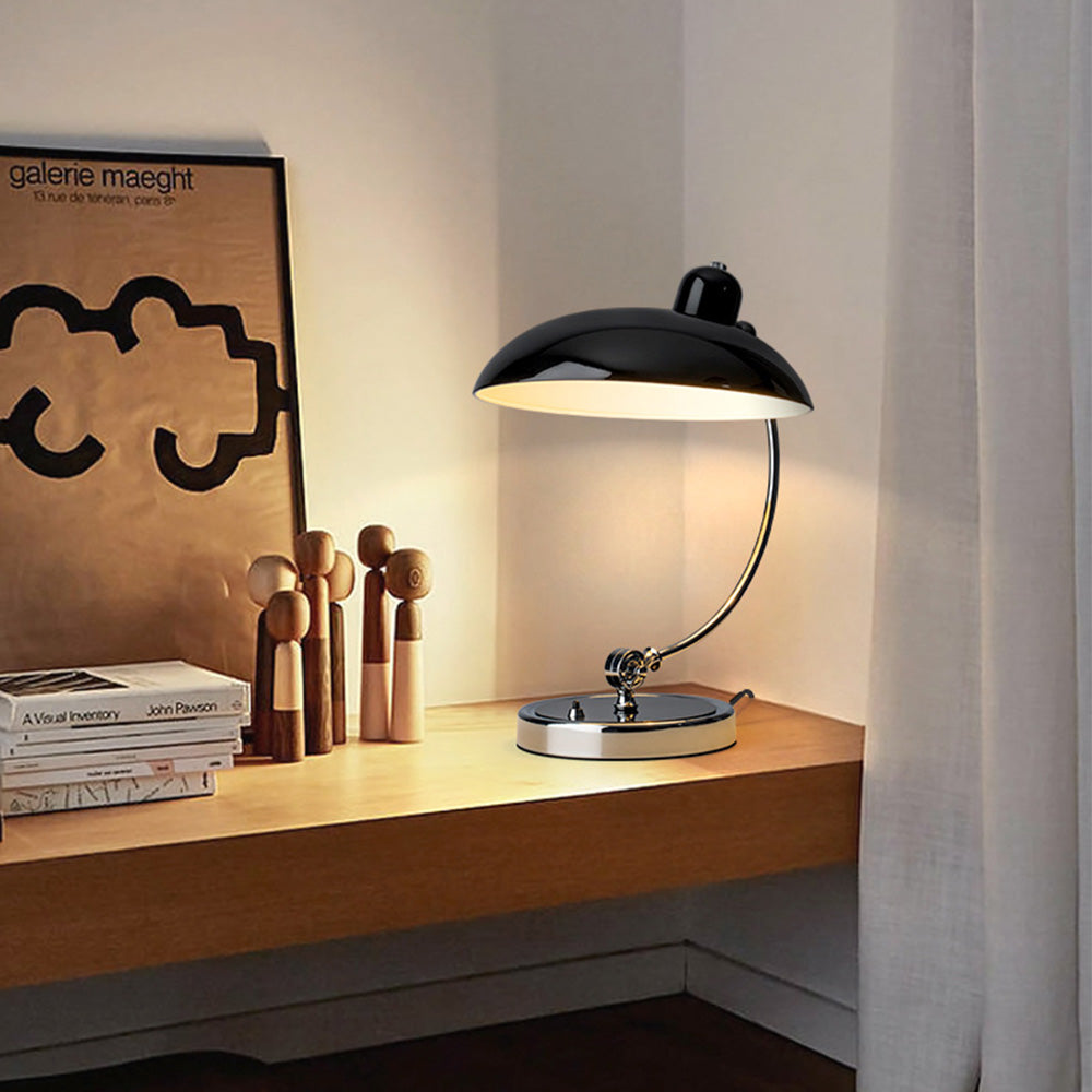 Black dome table lamp on a wooden shelf beside books, wooden figures and a tan framed print