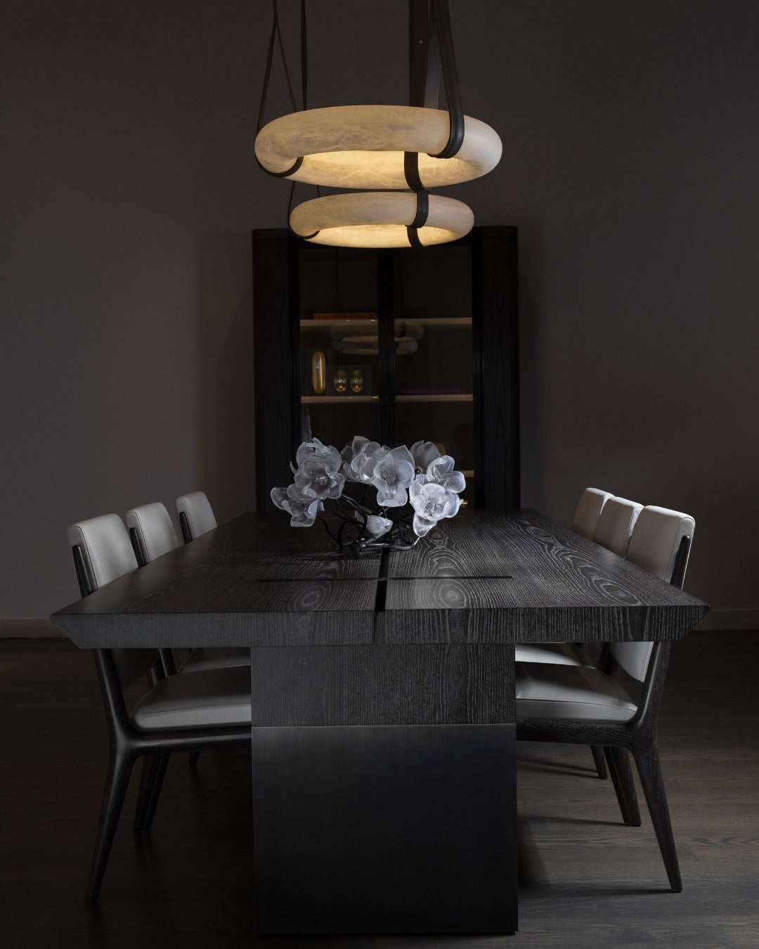 Two warm horizontal ring pendants above a dark rectangular dining table.