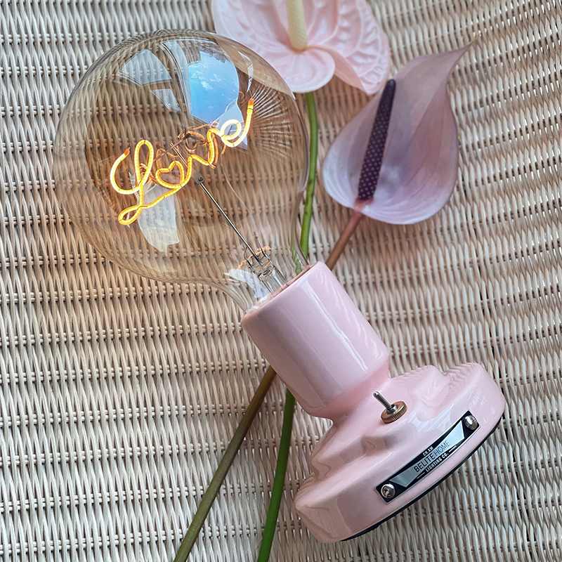 Tilted Love Pattern globe lamp with pink pedestal, small metal lever and heart-detail lettering near flowers and woven texture