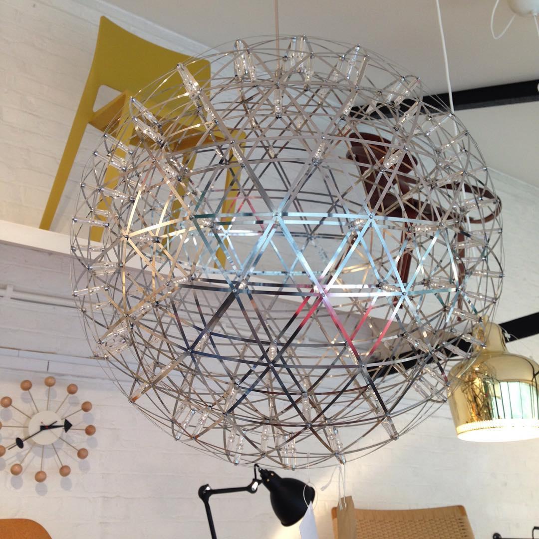Unlit lattice globe in a display area beside a wall clock, artwork and a black task lamp