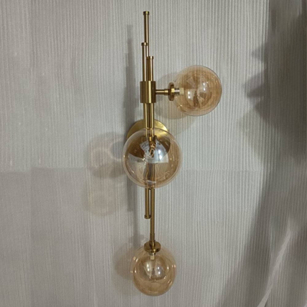 Unlit amber-tinted glass globes on gold-tone rods and a round wall plate near a finely striped pale curtain