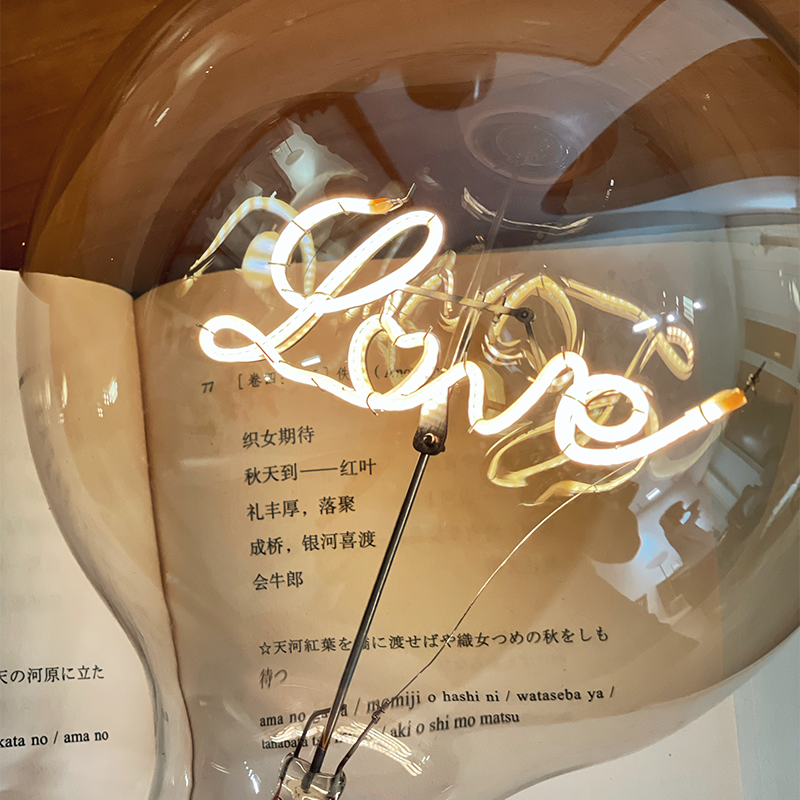 Close illuminated cursive Love and heart detail with support stem inside a transparent globe over an open book