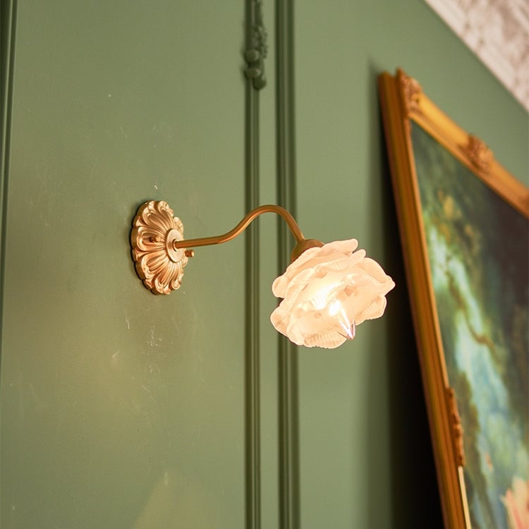 Flower wall light with curved arm on a green wall beside an ornate gold frame