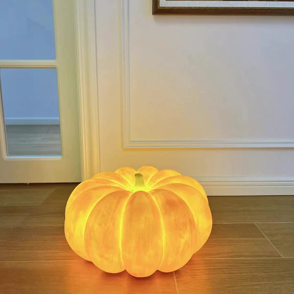 Glowing broad pumpkin lamp without a strap on wood floor beside a glass door and pale moulded wall