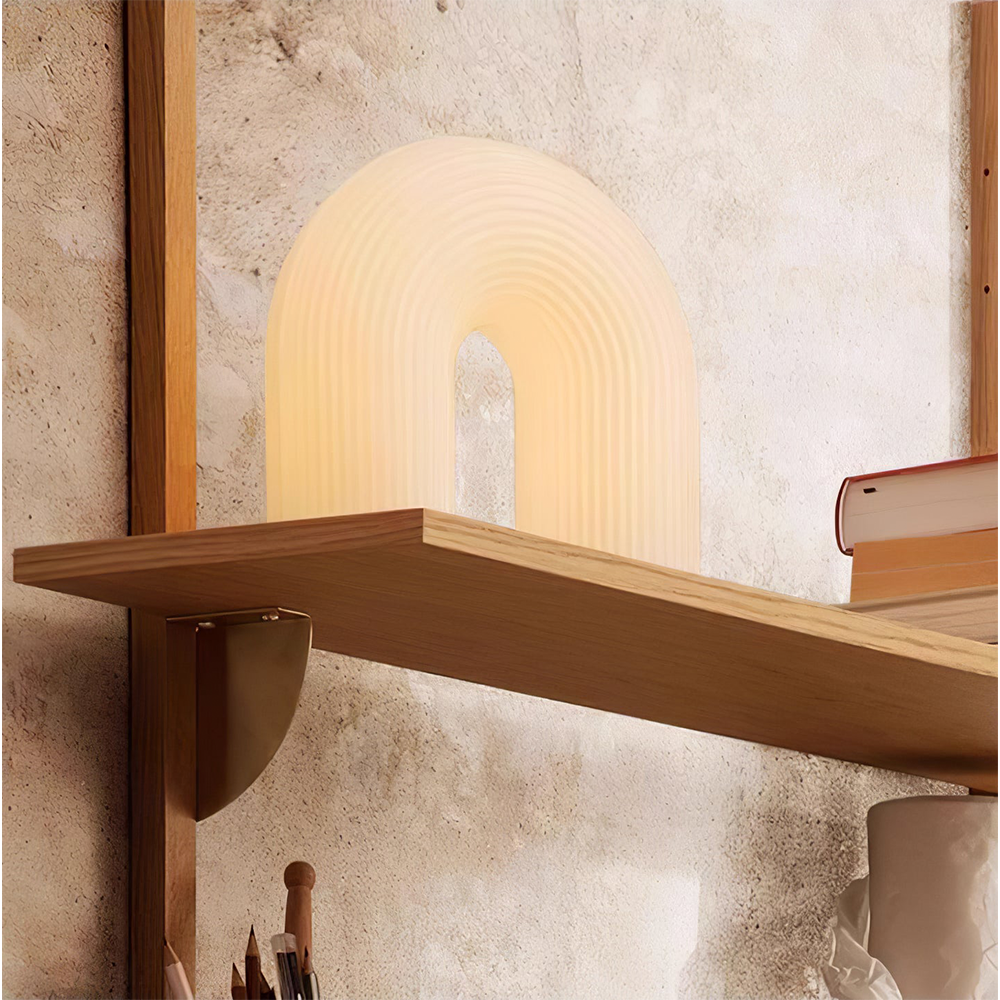Glowing Arch lamp partly behind a raised wood shelf edge against a textured cream wall