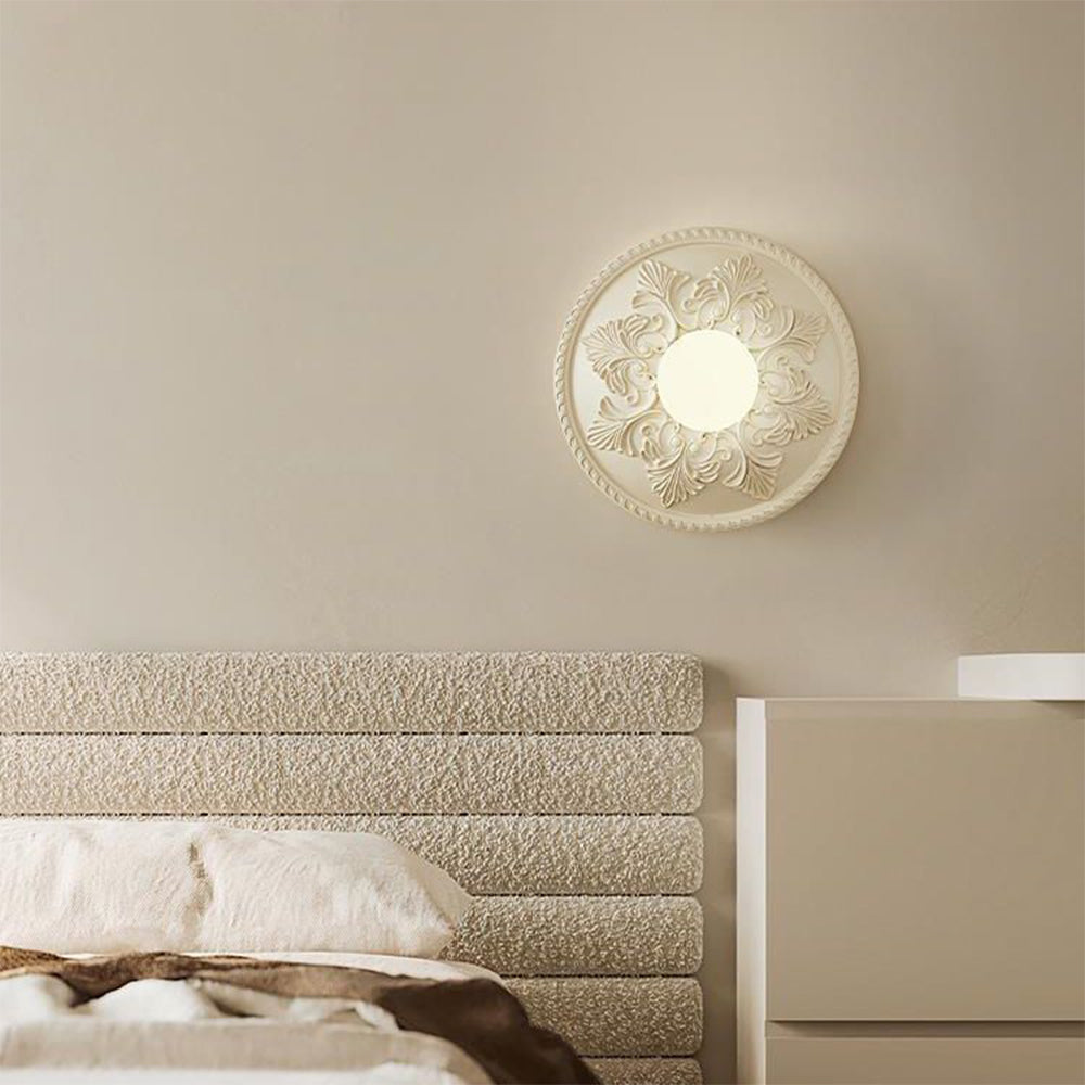 Cream relief globe wall light above a textured bed headboard and pale pillow