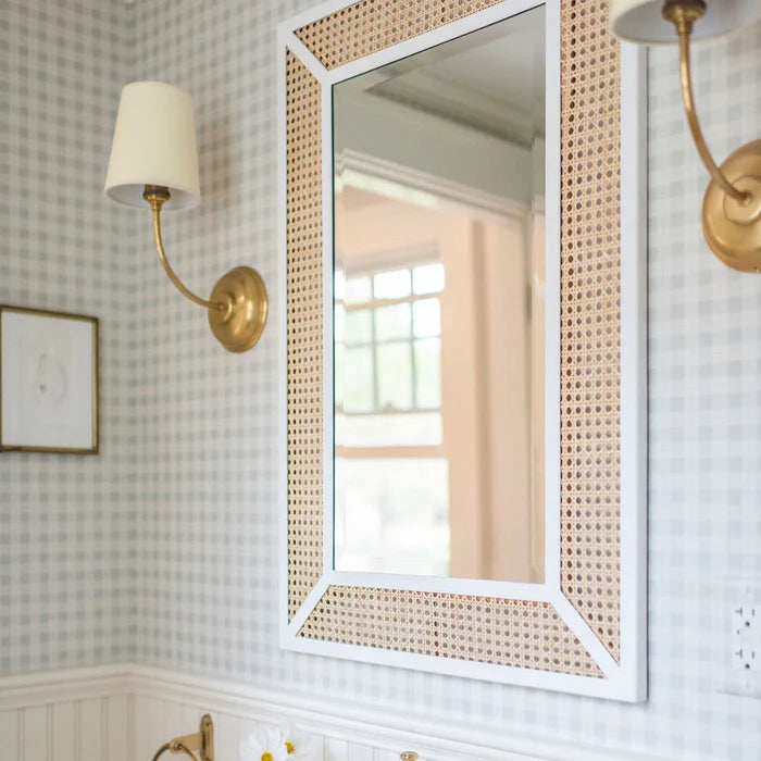 Close room view of brass curved-arm single wall lights beside a framed mirror.