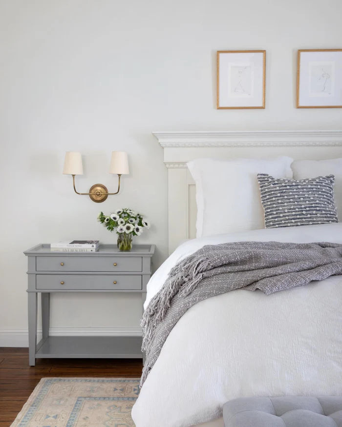 Brass double wall light above a grey bedside cabinet.