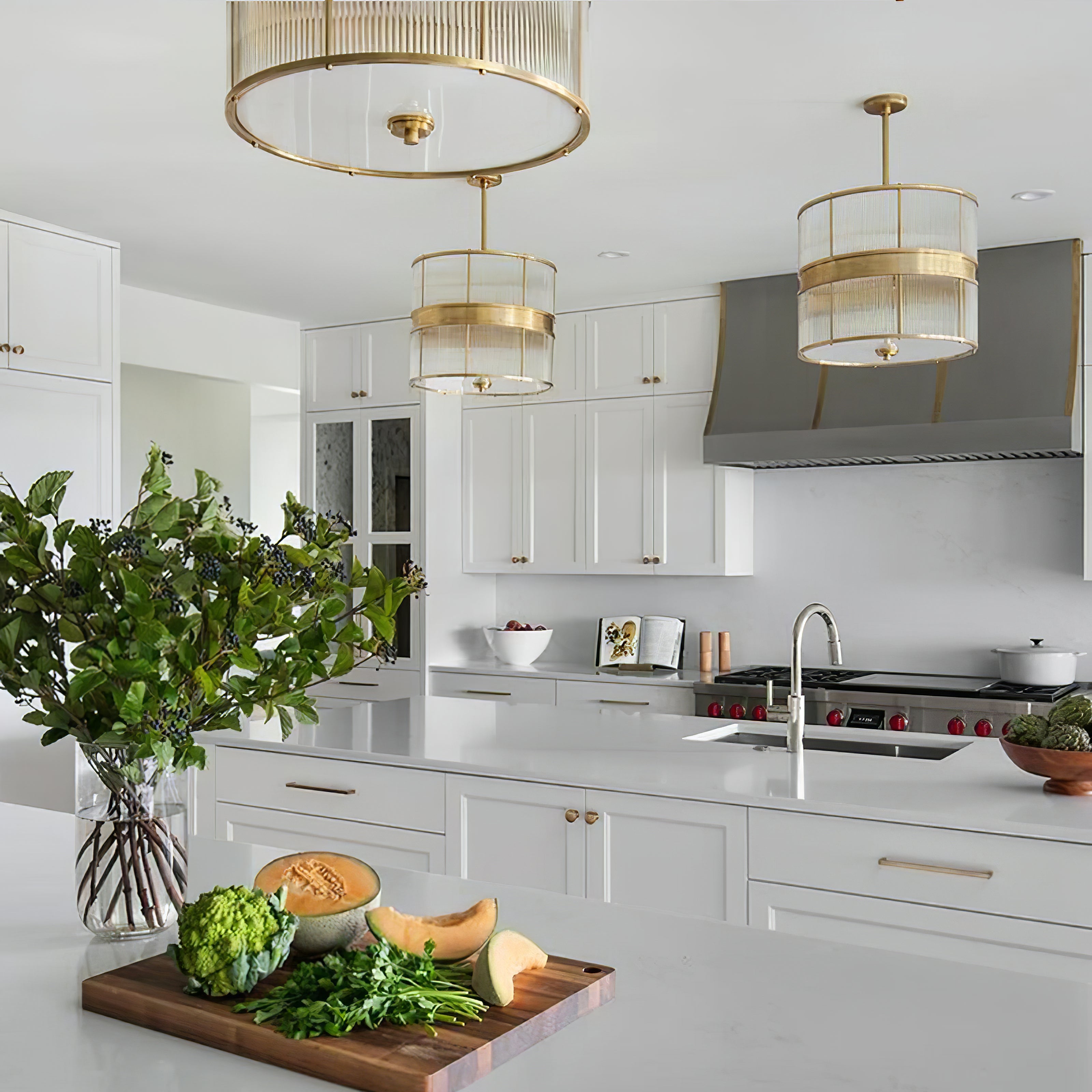 Low view of three bronze-tone drum pendants showing round lower diffusers above a white kitchen island