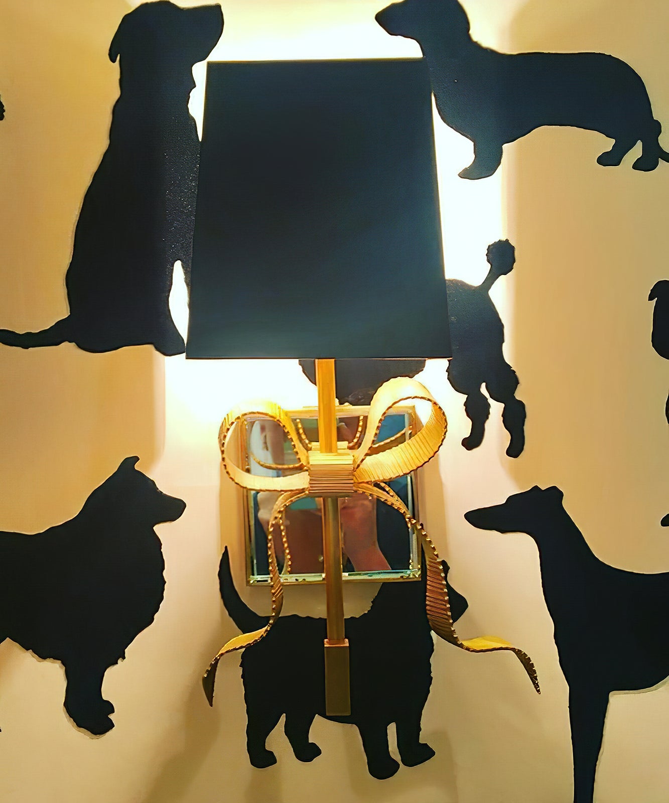 Black-shade brass-tone bow light glowing against wallpaper patterned with dark dog silhouettes