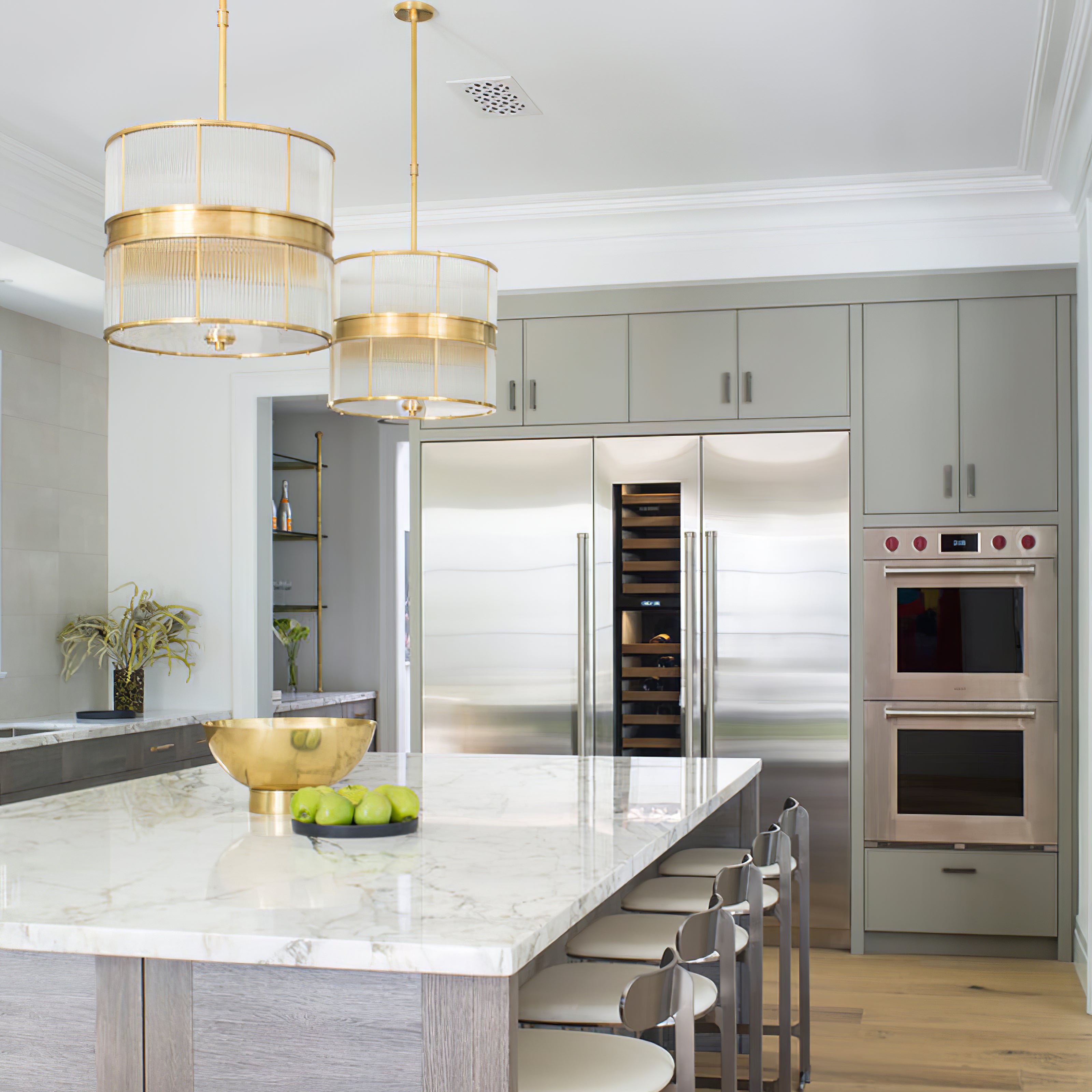 Two bronze-tone glass-rod drum pendants over a marble kitchen island with stools and a wine cooler behind