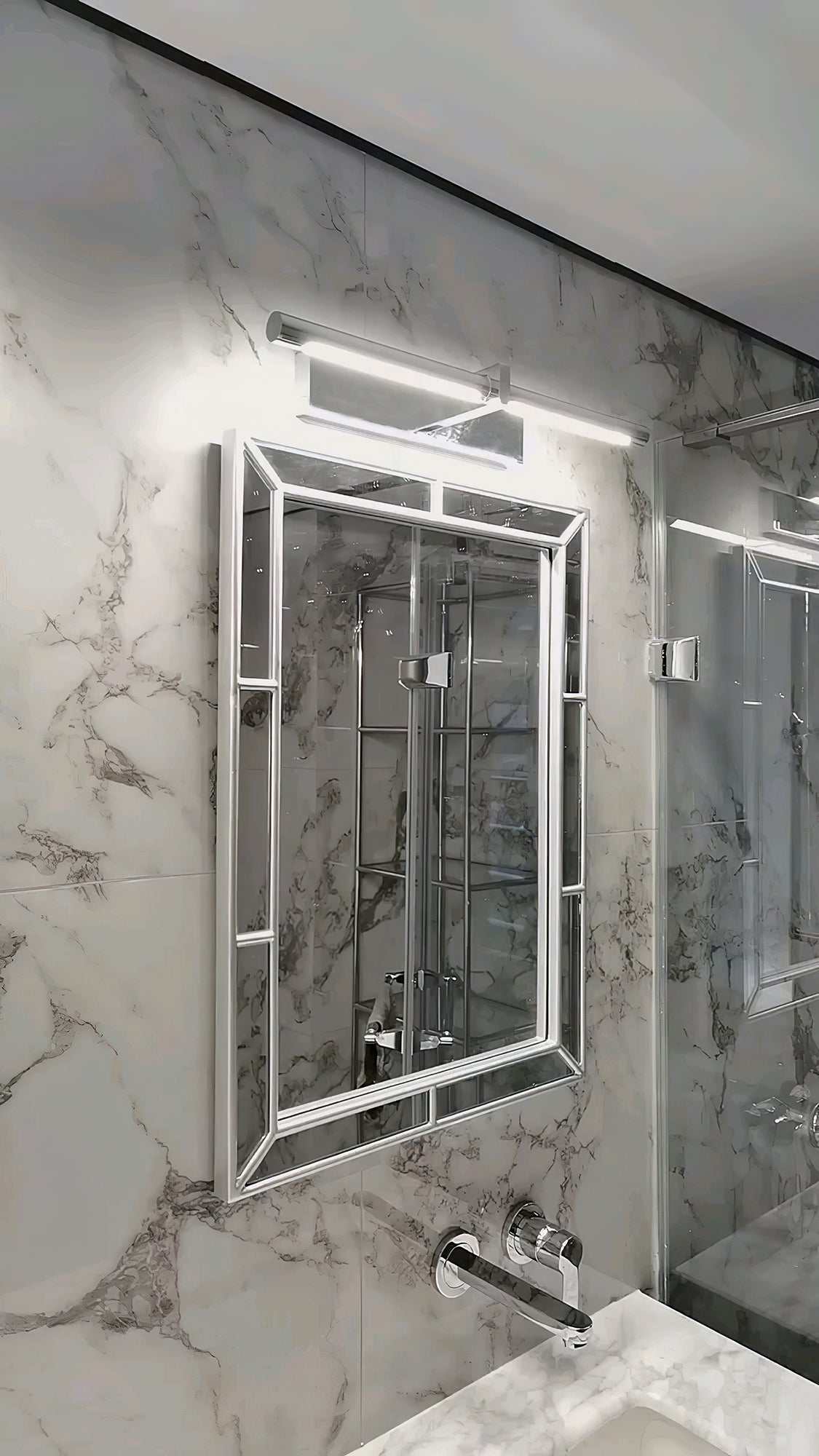 Close silver-colour picture light above a bevelled mirror on a marble wall beside a basin and taps