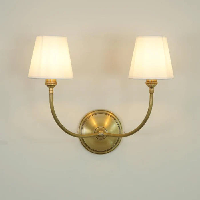 Illuminated brass double wall light with rounded backplate on a pale wall.