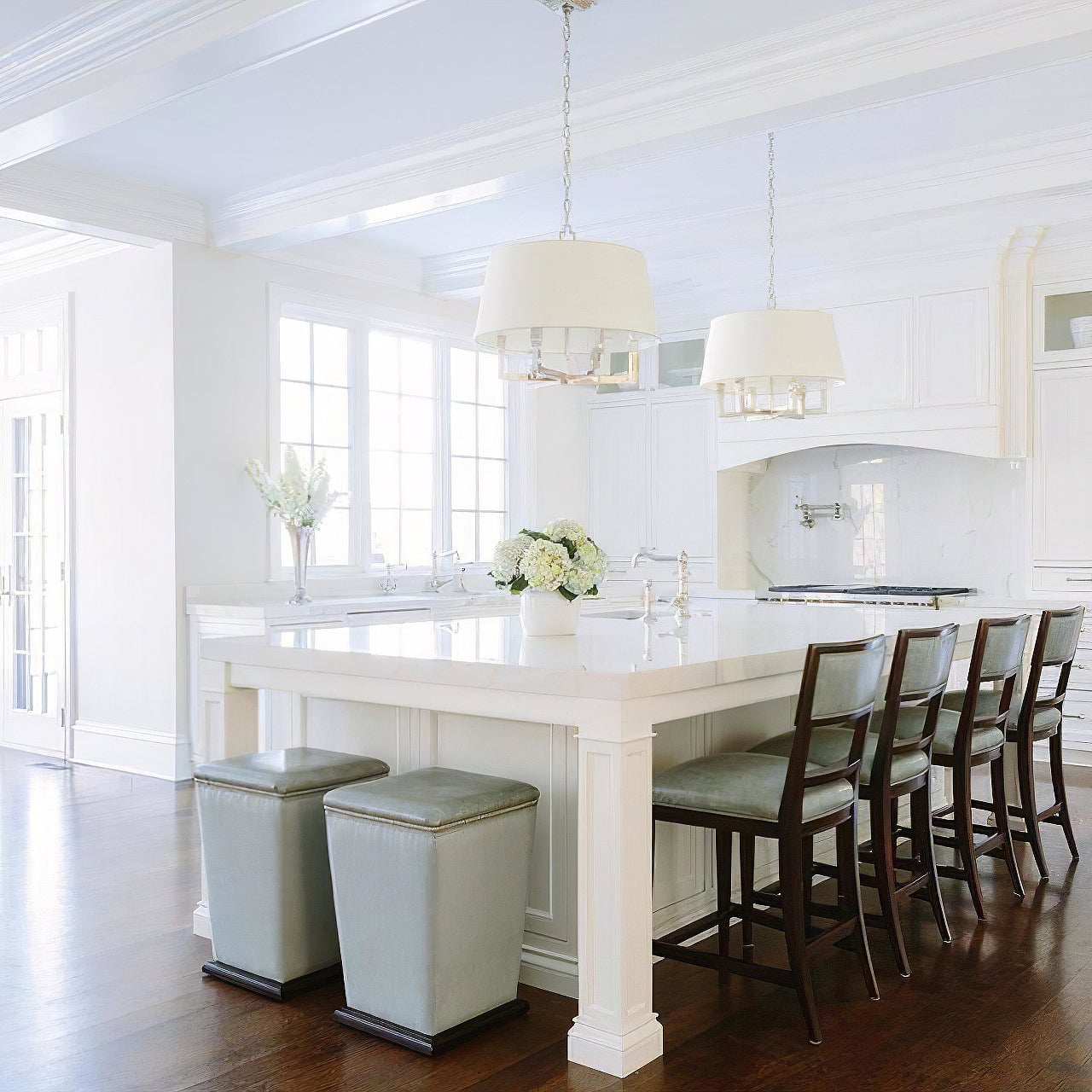 Angled kitchen view of two silver-looking shaded chandeliers over an island with grey bar stools
