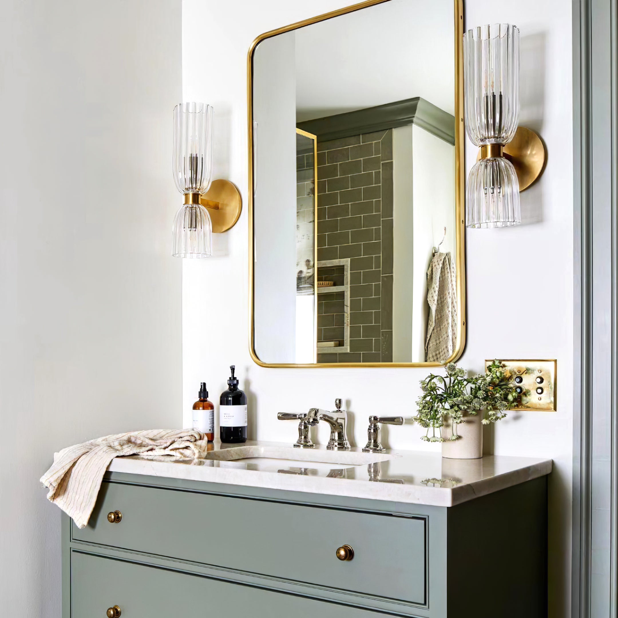 Pair of Antique Brass-tone double glass sconces beside a gold-trimmed mirror above a green bathroom vanity