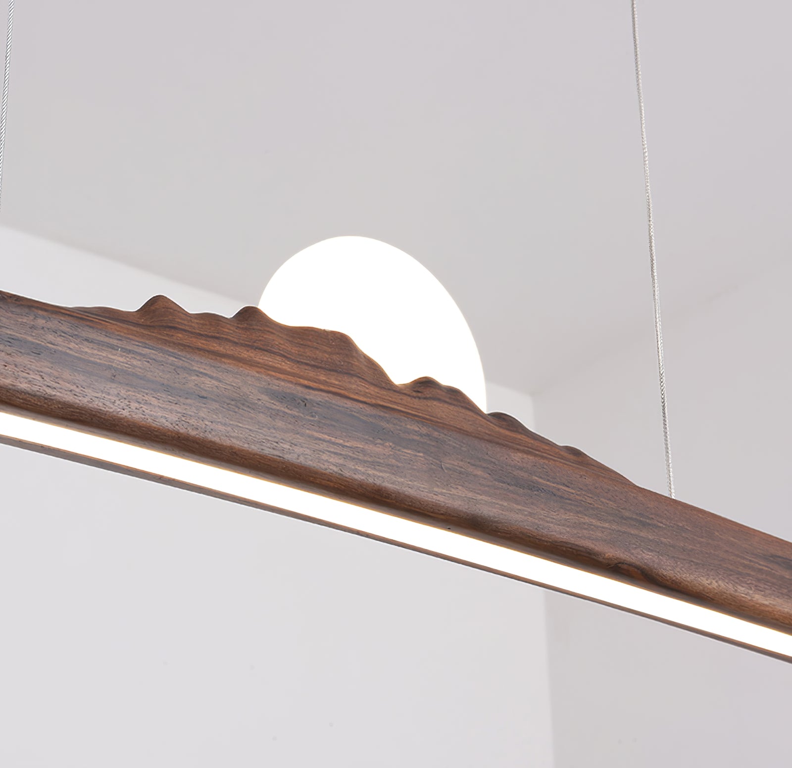 Angled close-up of the dark wood ridge, glowing globe-like element, luminous underside and thin cables