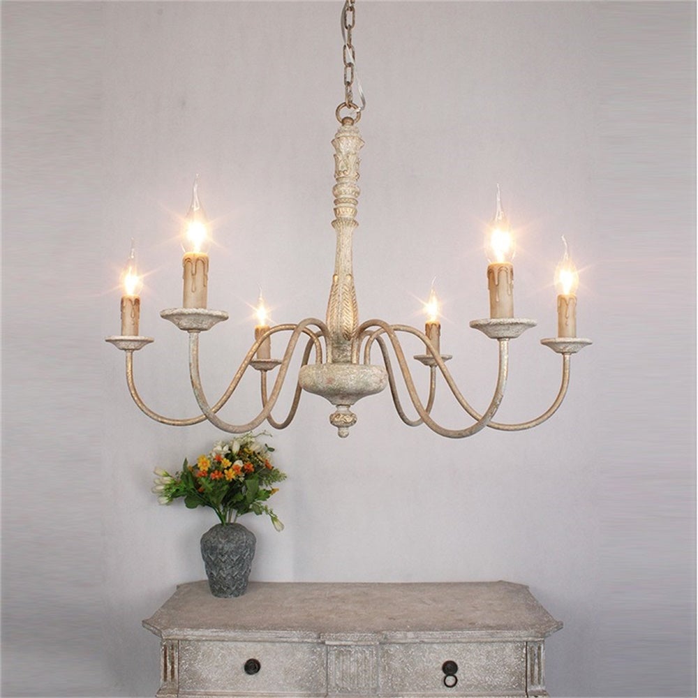 Ornate pale six-light chandelier with drip-effect candle sleeves above a distressed cabinet and flower vase