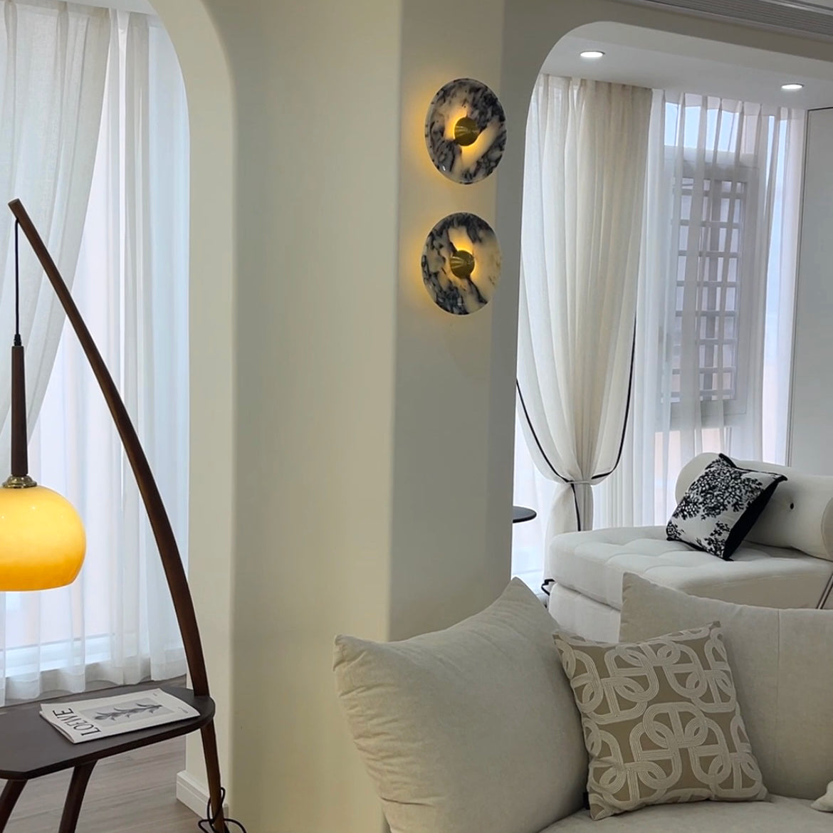 Two Gold-centred veined stone wall lights on a living-room column beside white curtains and a sofa