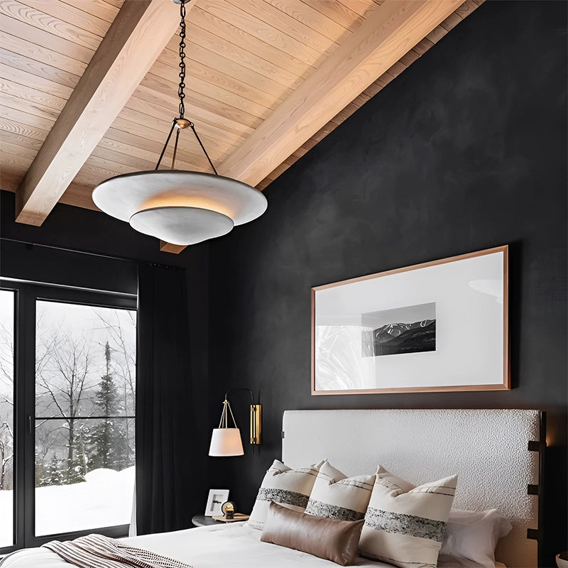 Illuminated white Mollino tiers and black suspension beneath wooden ceiling in dark bedroom beside framed art