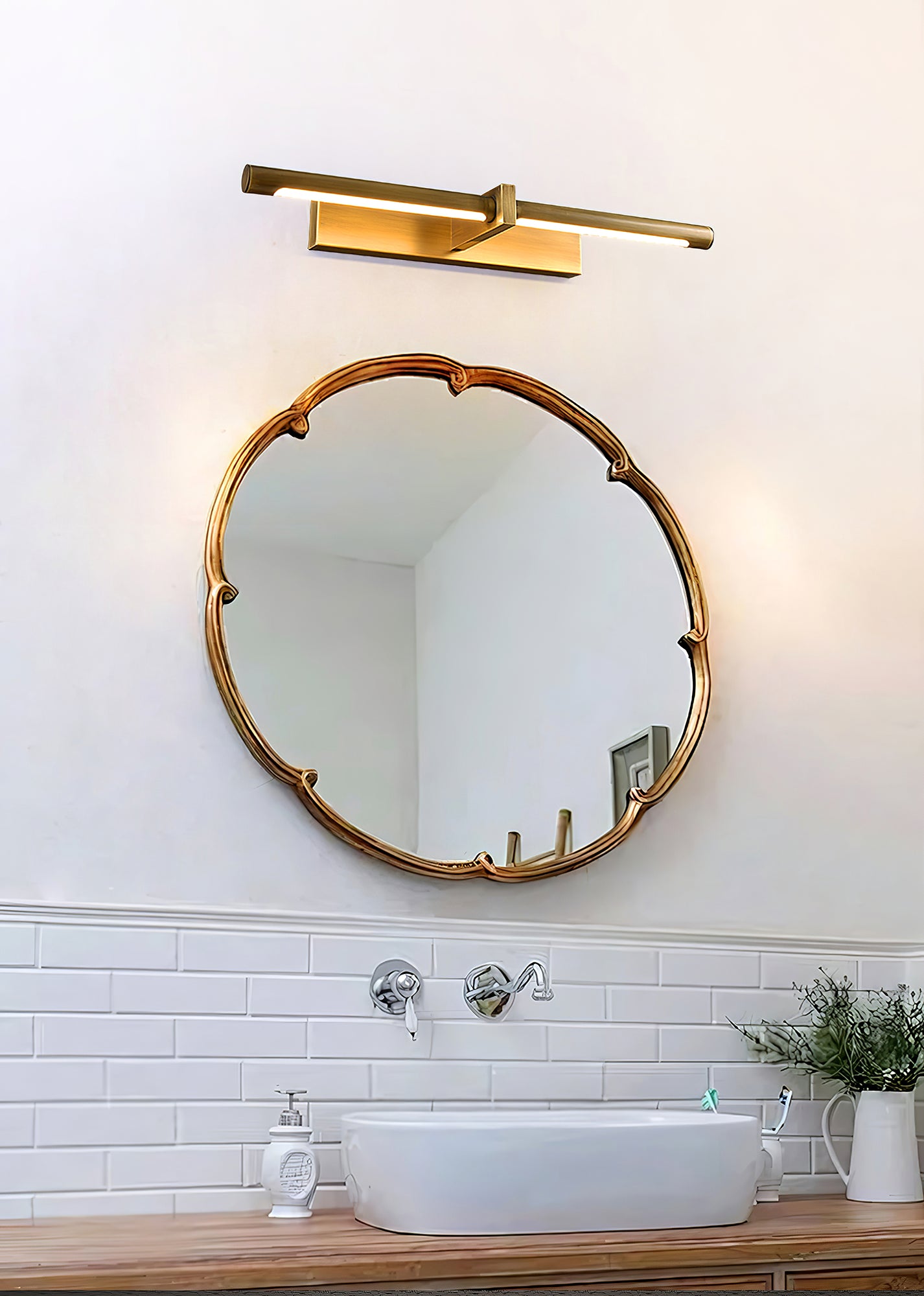 Brass-colour picture light above an ornate round mirror and basin beside a tiled wall and plant