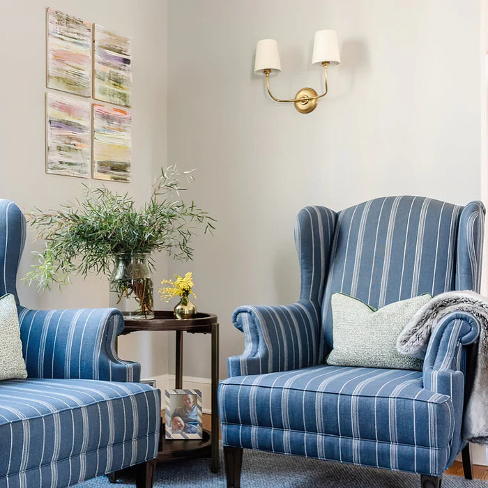 Brass twin-shade wall light above blue striped armchairs.