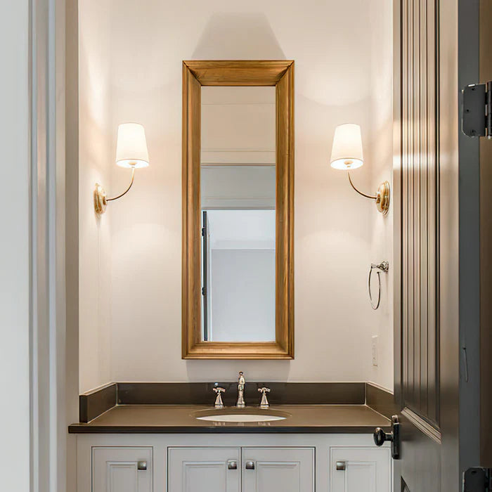 Brass single wall lights on either side of a tall narrow vanity mirror.
