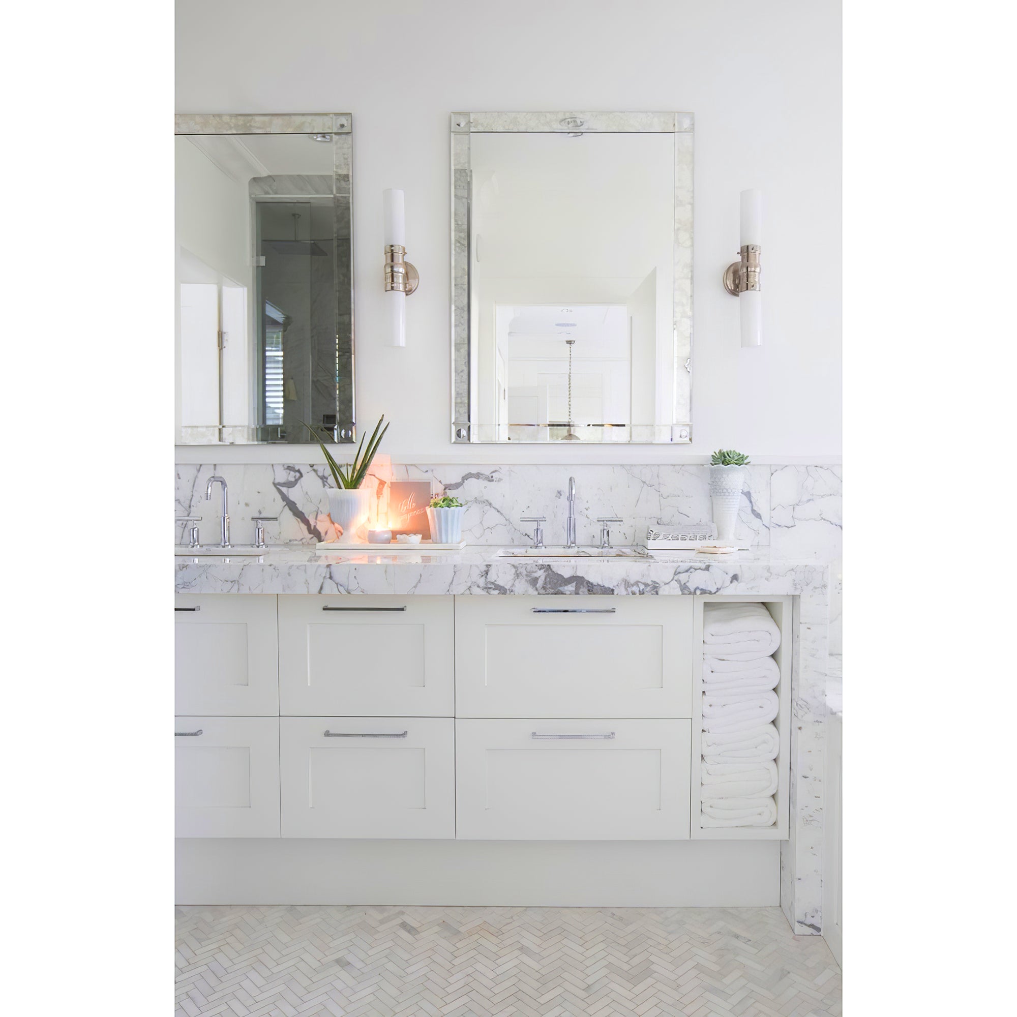 Silver-tone double white-glass wall lights at large bevelled mirrors above a white vanity and veined counter