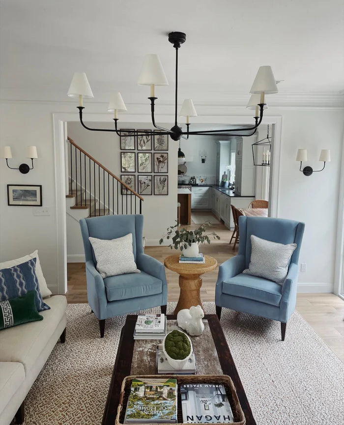 Shaded wall lights in a sitting room with blue chairs and a black chandelier.