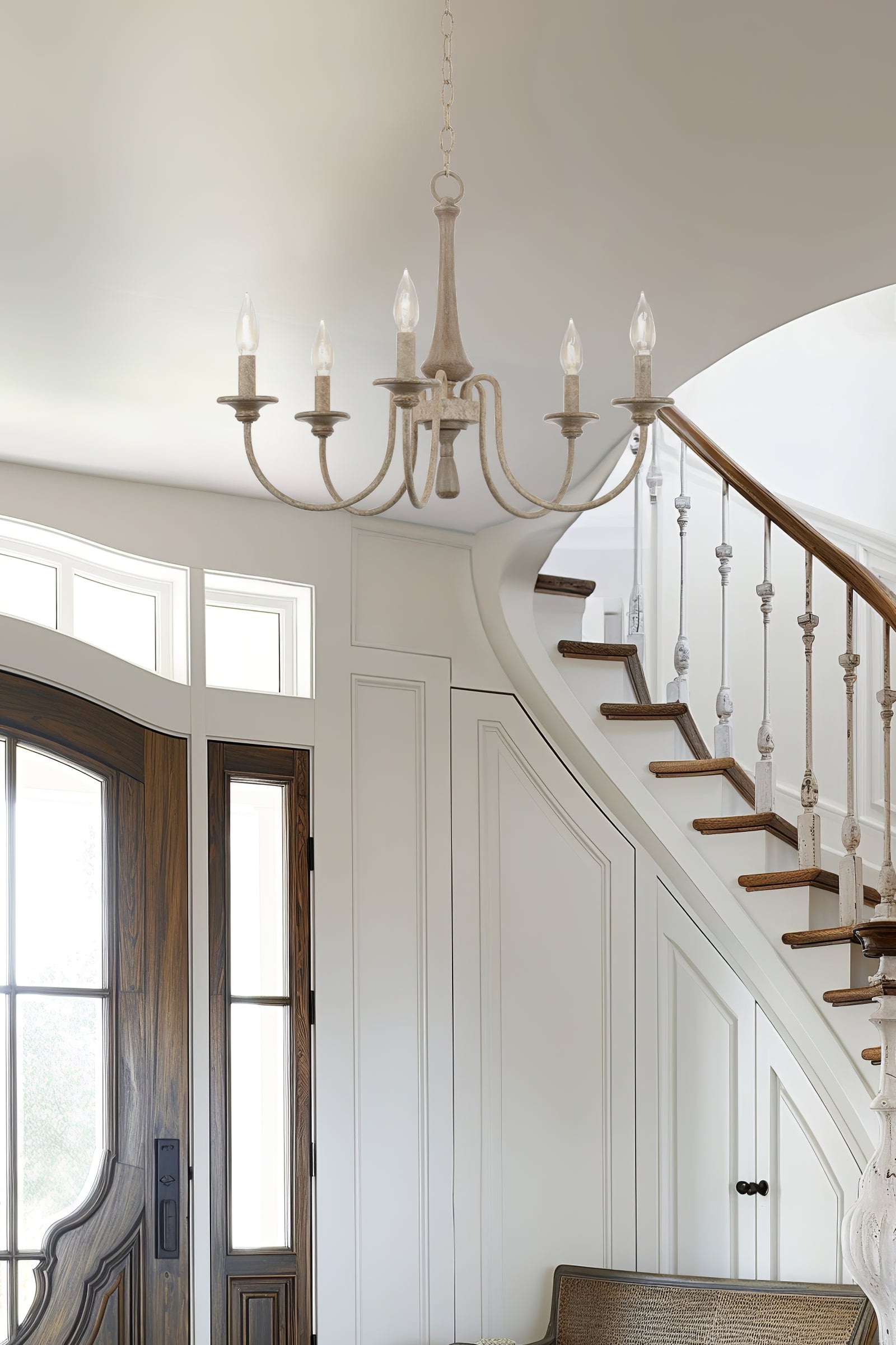 Pale five-light chandelier near a curved white staircase, wooden treads and dark entrance door
