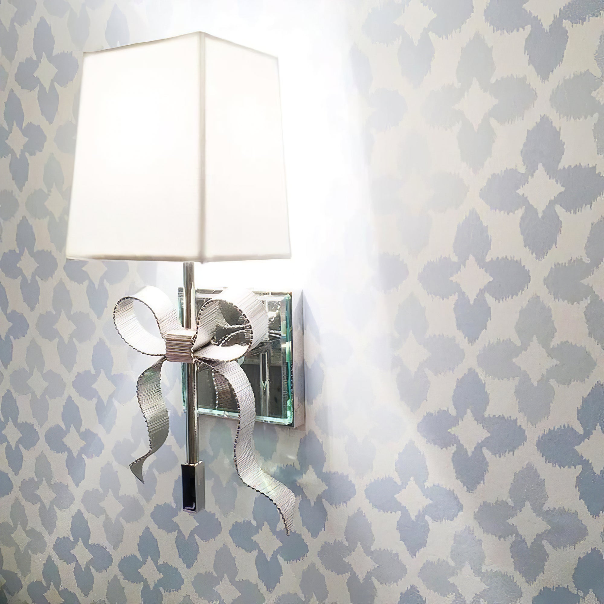 Polished Nickel bow wall light with pale rectangular shade and curled ribbon tails against pale blue patterned wallpaper