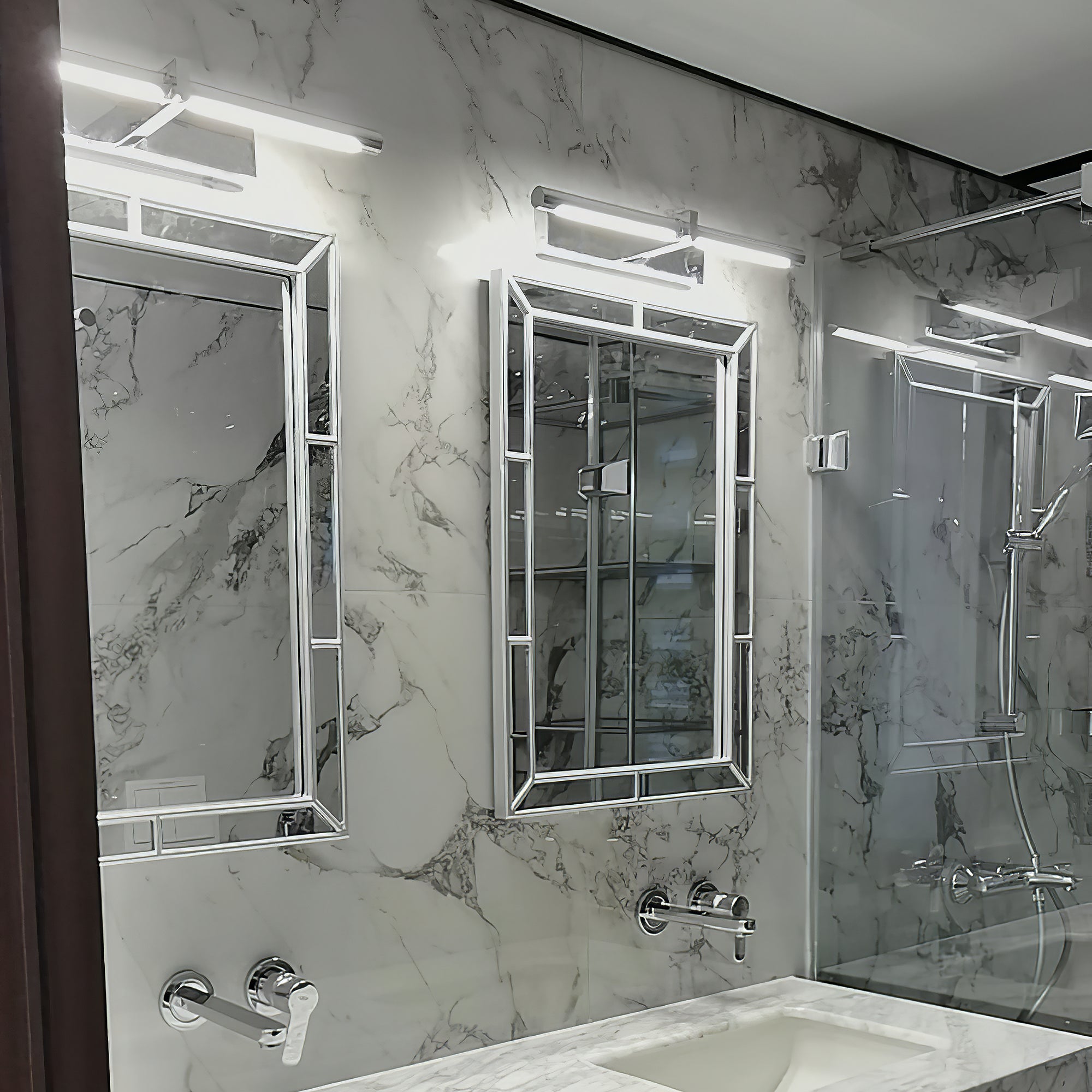 Silver-colour picture lights above bevelled rectangular mirrors and a marble vanity