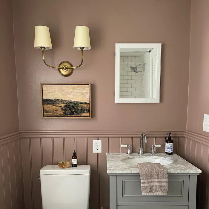 Brass double wall light above artwork in a room with mauve panelling.