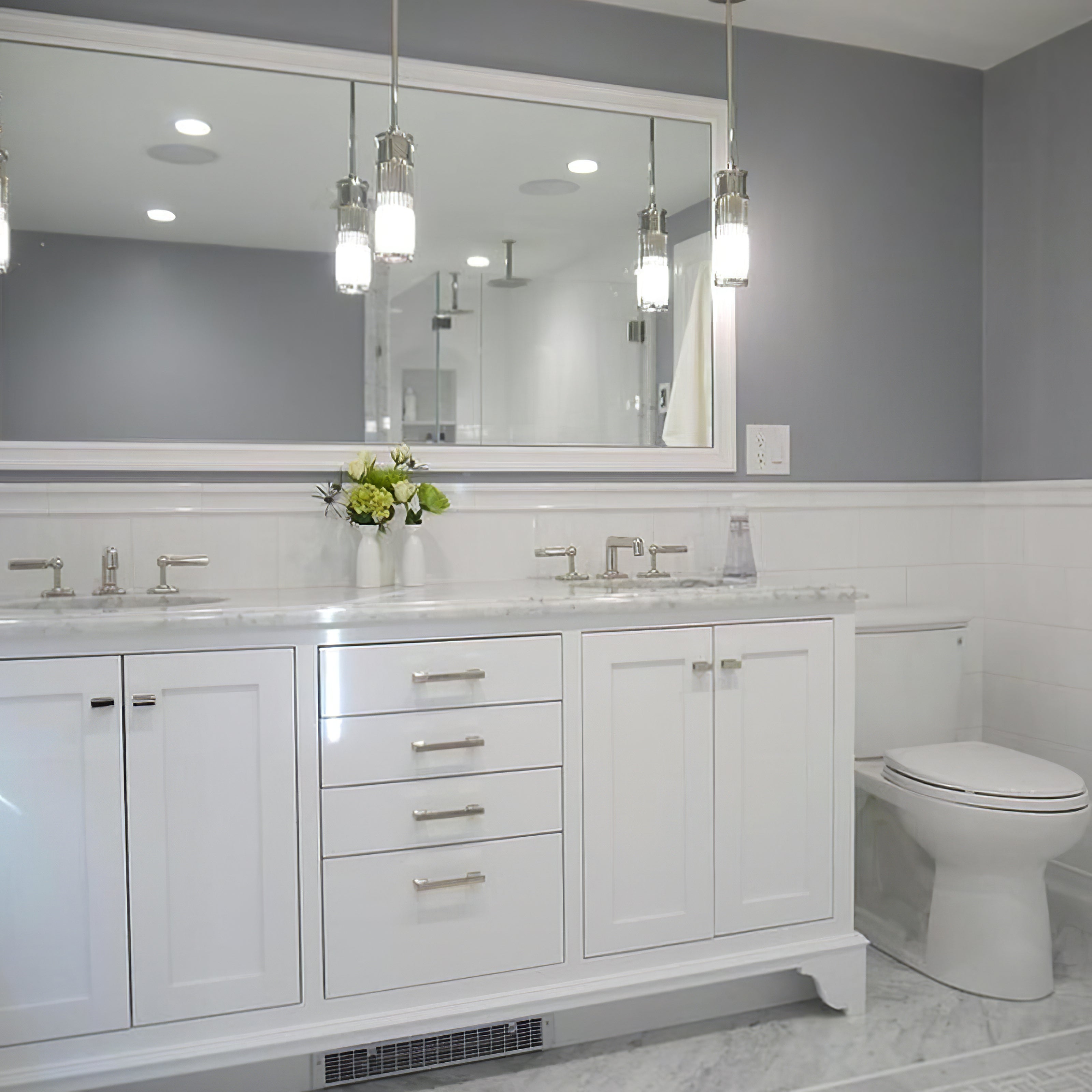 Two slender silver-tone glass pendants at a bathroom double vanity, with reflections in the mirrors