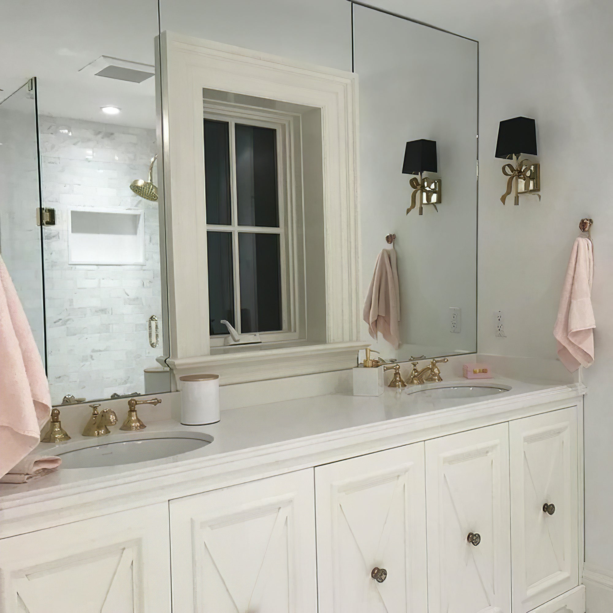 Black-shade brass-tone bow light and its reflection beside a large mirror above a white double-basin cabinet