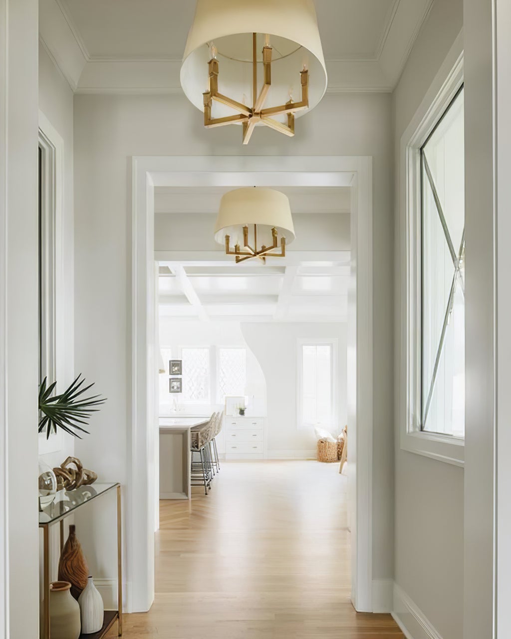 Low-angle view of angular gold-toned candle arms beneath a round shade, with another chandelier beyond a doorway