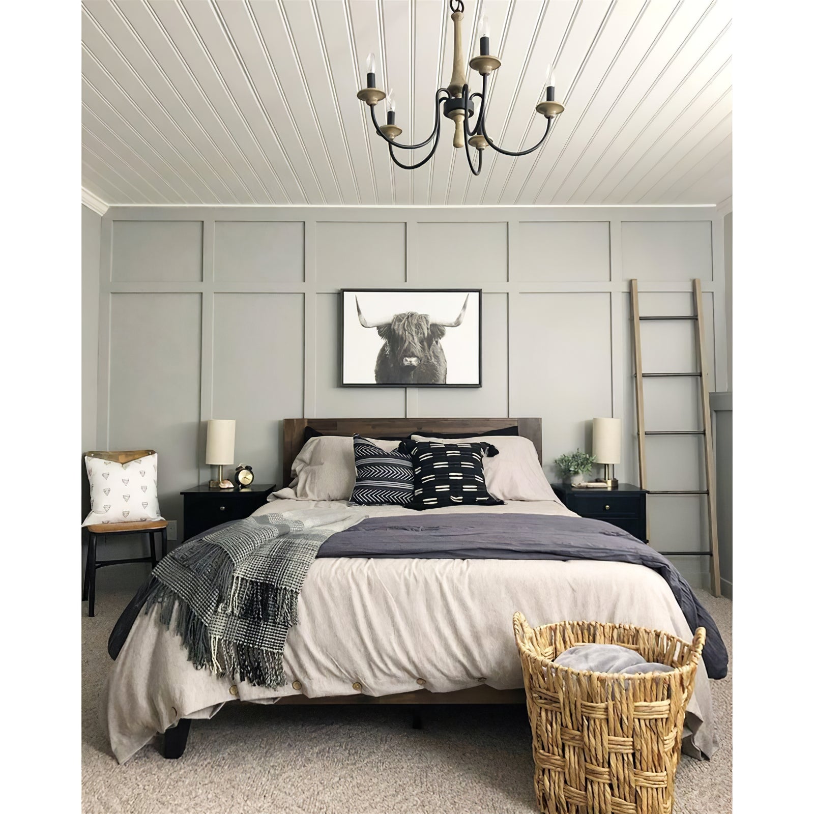 Wood-toned chandelier with black arms above a bed beneath a paneled ceiling and framed cattle picture