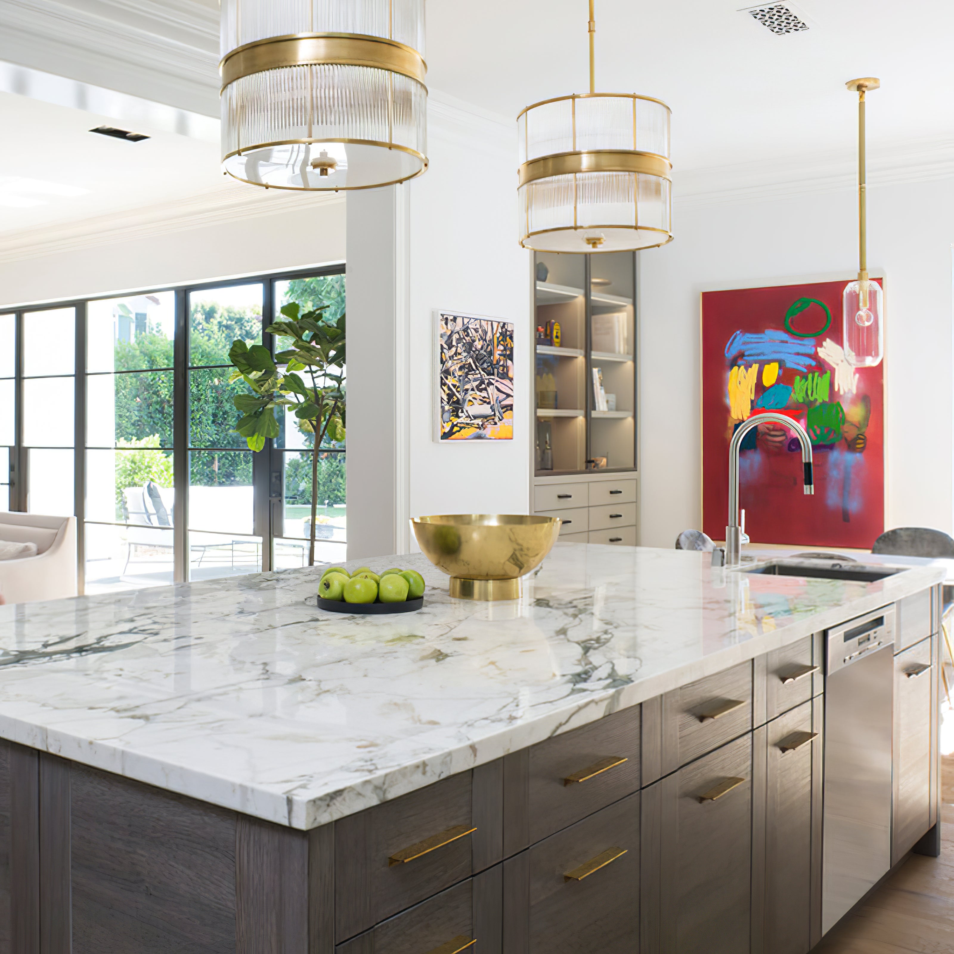 Bronze-tone drum pendants over a kitchen island with a separate slender glass pendant beside red artwork