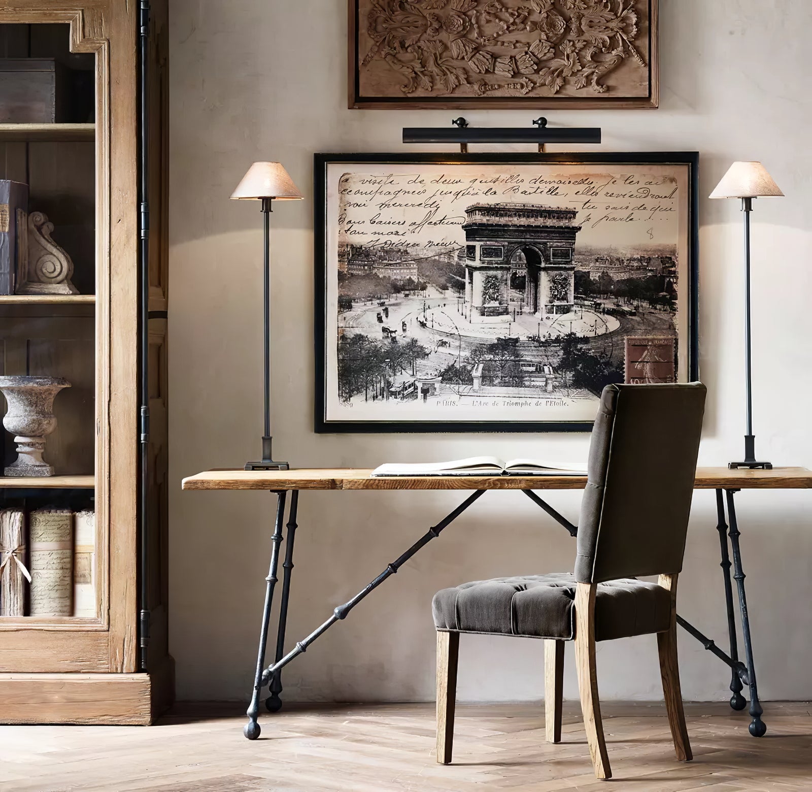 Two Black Slim Candlestick lamps with cream shades on wooden desk flanking framed artwork behind open book and upholstered chair