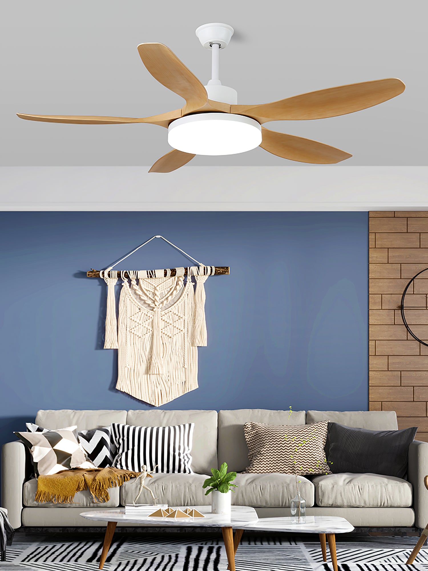 Wood-tone five-blade fan with white housing above a grey sofa, blue wall and cream textile hanging
