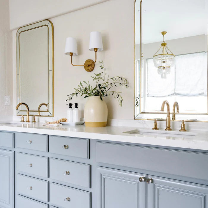 Brass double wall light between tall mirrors above a blue vanity.