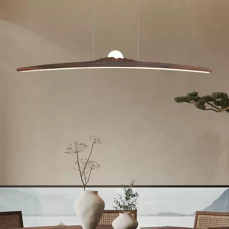 Dark curved bar pendant with a glowing centre above a dining table, ceramic vases and woven chairs
