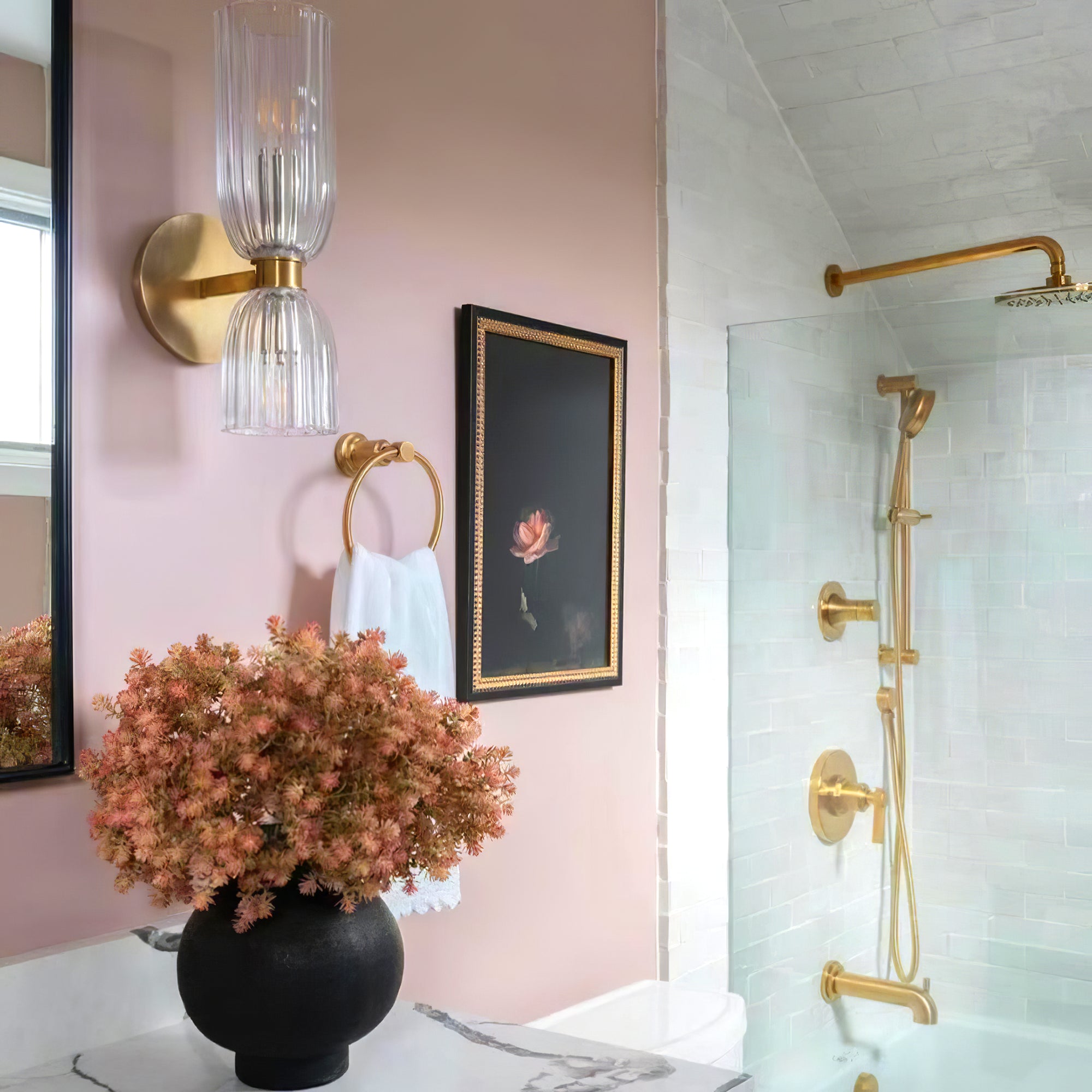 Double ribbed glass wall sconce on a pink wall beside a black mirror edge and a glass shower enclosure