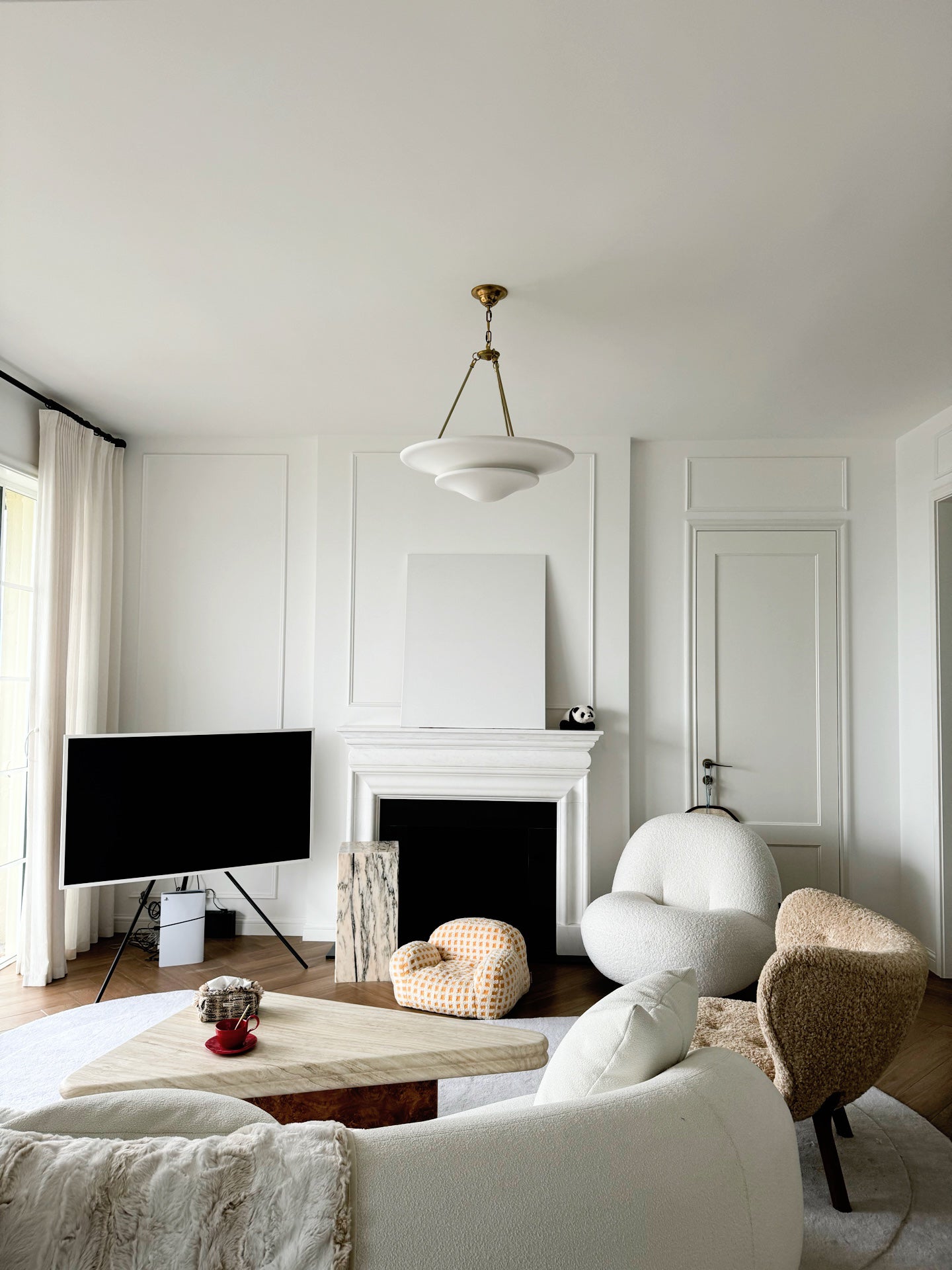 Mollino white two-tier chandelier above living room coffee table beside fireplace, TV and upholstered seating