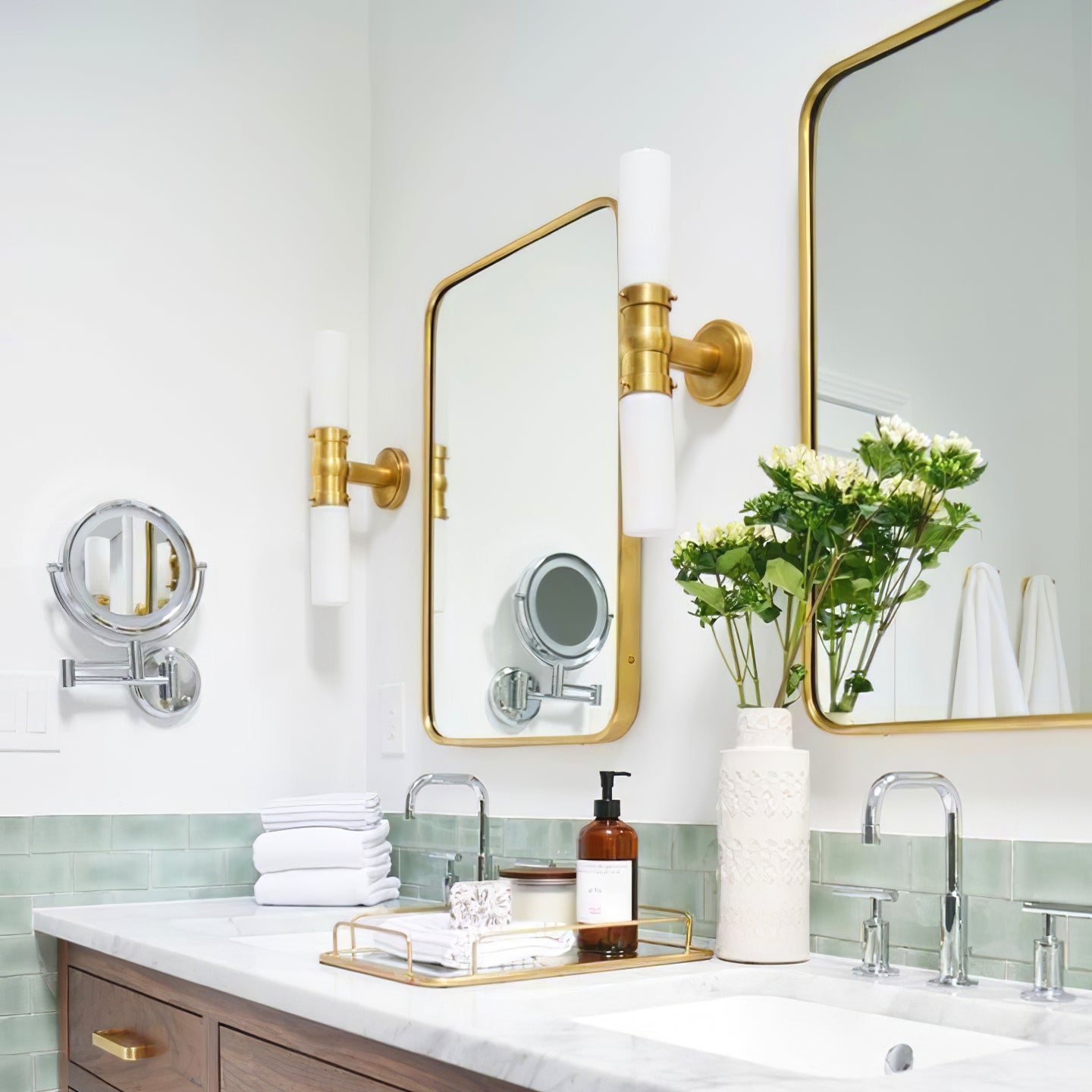 Brass-tone double glass wall lights beside gold-trimmed bathroom mirrors above a wood vanity and green tiles