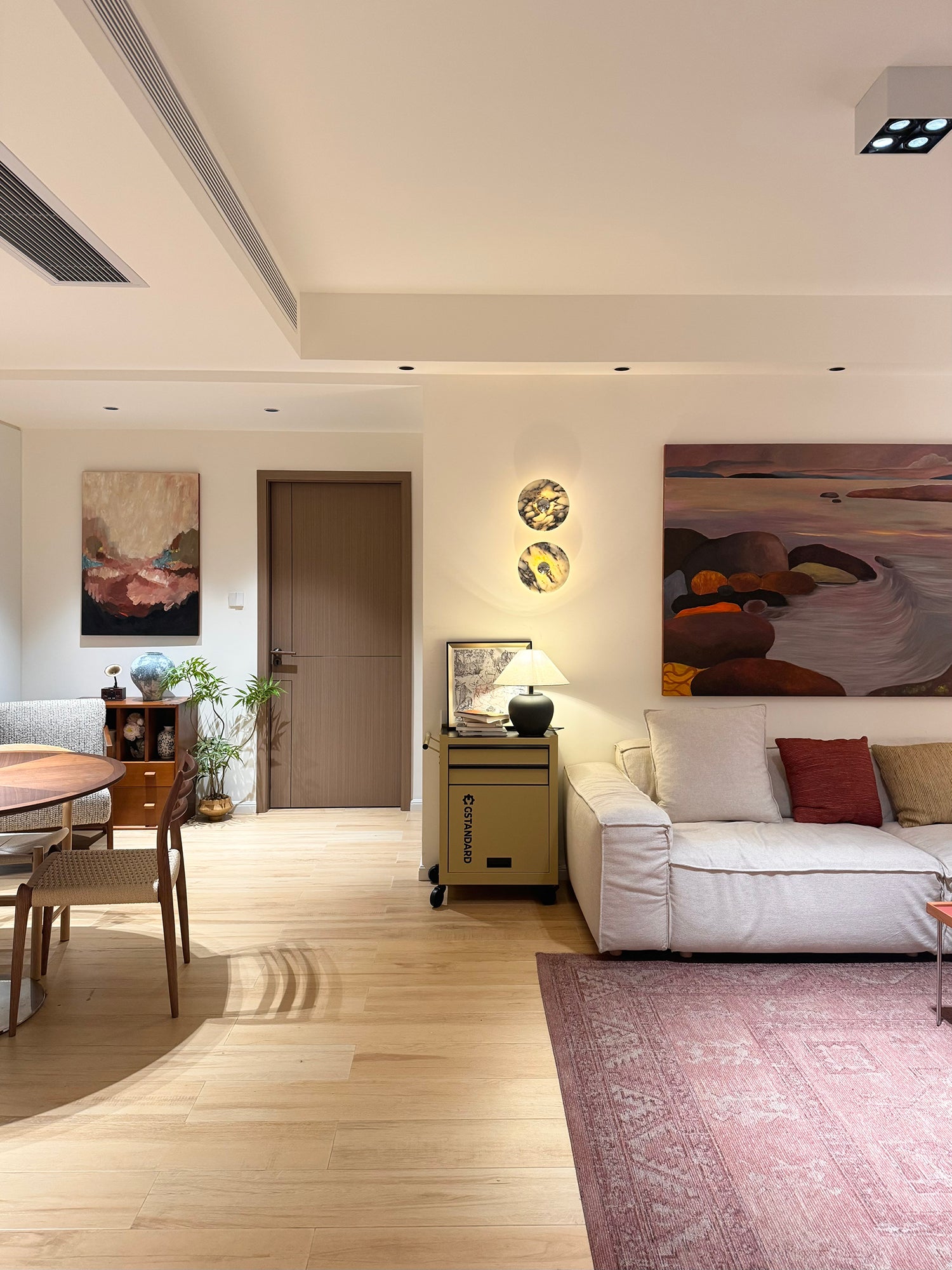 Living and dining room view of two glowing stone wall lights between a wood door and a landscape painting