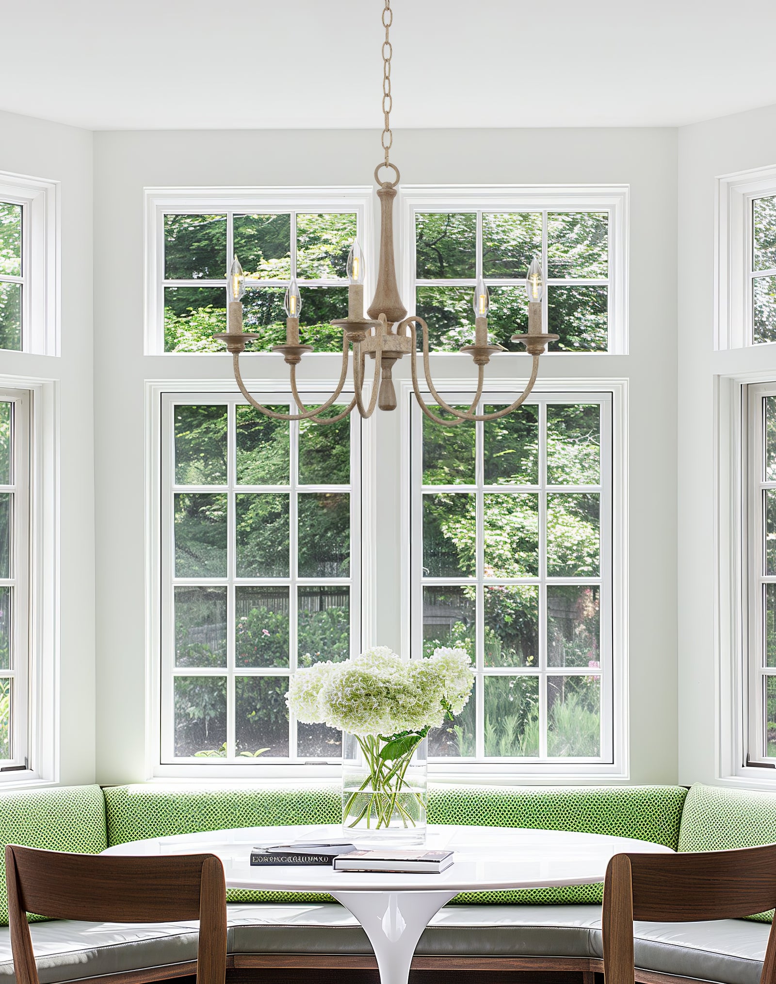 Pale five-light chandelier above a round white table beside a green window bench and flowers