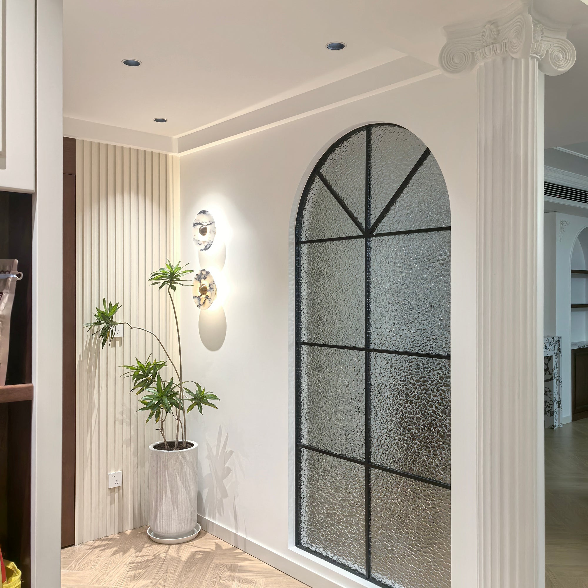 Wide view of paired Gold-centred stone wall lights with a potted plant, wall slats and an arched glass partition