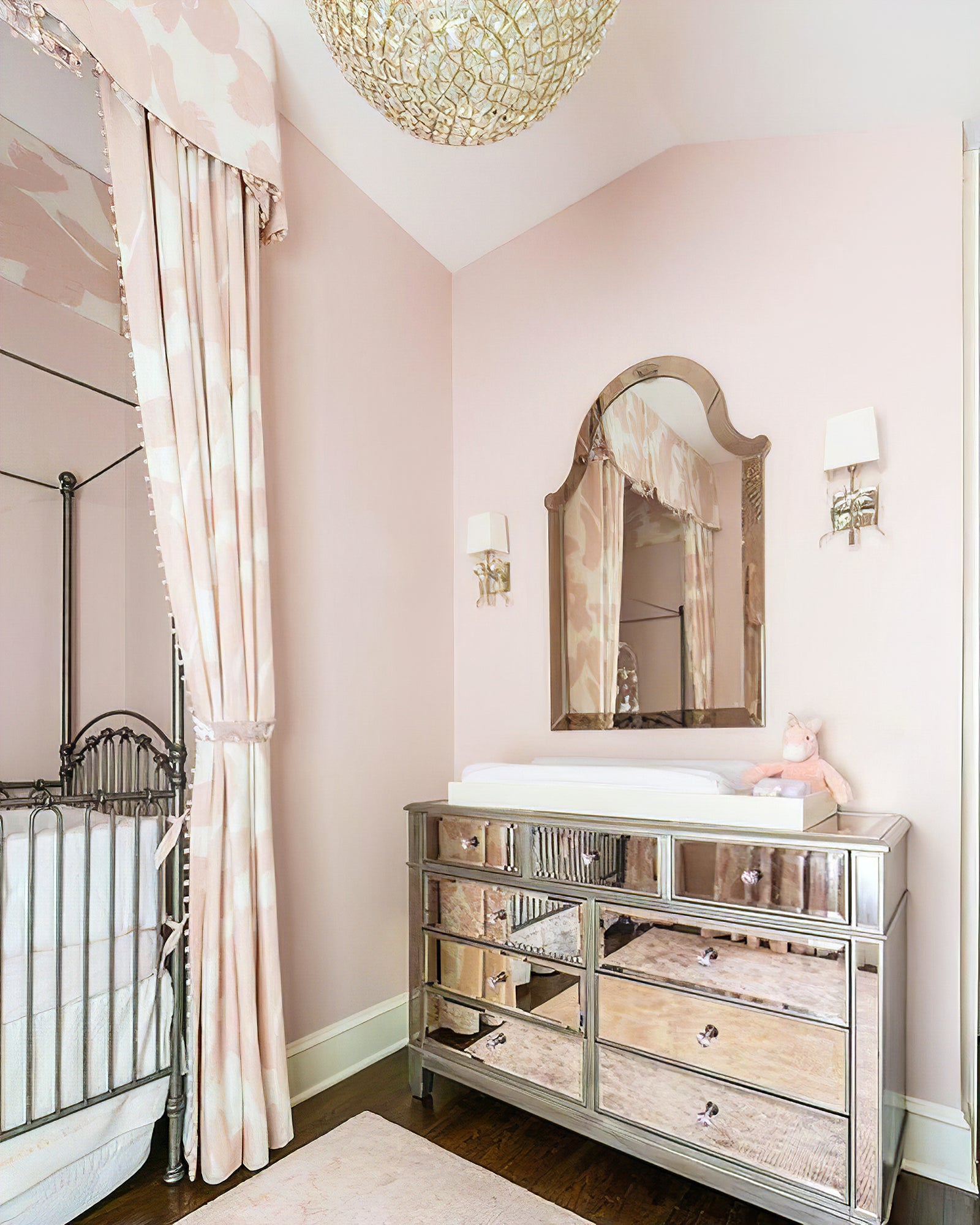 Two pale-shade bow lights flanking a shaped mirror above a mirrored chest in a pink bedroom setting